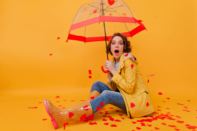 雨伞惊喜的热情女孩穿着橡胶秋鞋坐在地板上摄影棚里快乐的女模特摆姿势 围在纸心上阳伞情绪女人