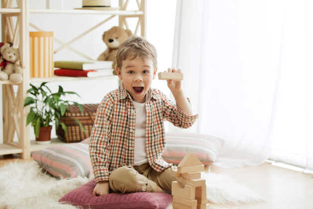 幼儿园坐在地板上的小孩在家里玩木块的男孩面带微笑 很惊讶房子男孩塔楼