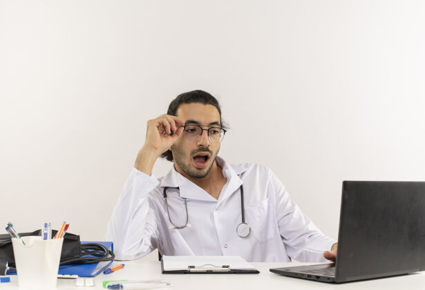 工作惊讶的年轻男医生戴着医用眼镜 穿着带听诊器的医用长袍年轻男性惊喜