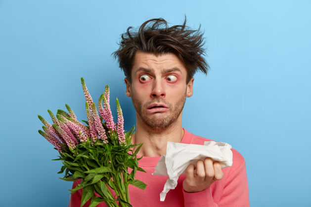 疾病惊呆了的男人睁大眼睛盯着植物 头发凌乱 一直拿着餐巾纸打喷嚏 对花粉和花有过敏反应 生病感到恶心和疲惫鼻子手帕治疗