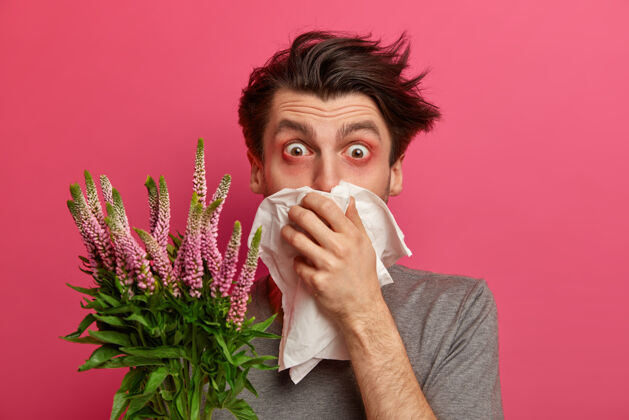 医学有过敏症状的人打喷嚏 用餐巾捂住鼻子 听过敏症医生的建议如何治疗花粉热 眼睛红润 需要治疗过敏性鼻炎 隔离在粉红色的墙上室内感冒单色