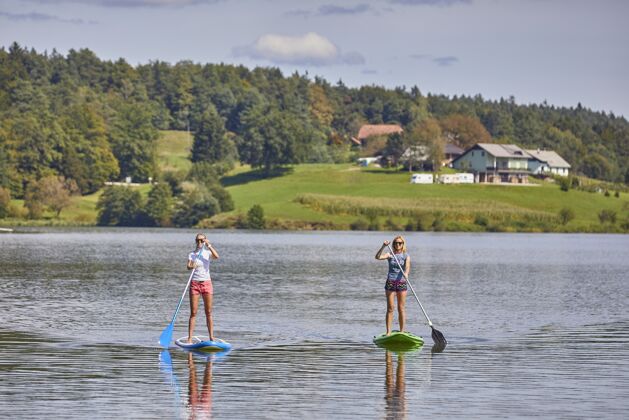 海洋在斯洛文尼亚的斯马特因斯科湖上 两个女人骑着一个独立的桨板娱乐动作划桨