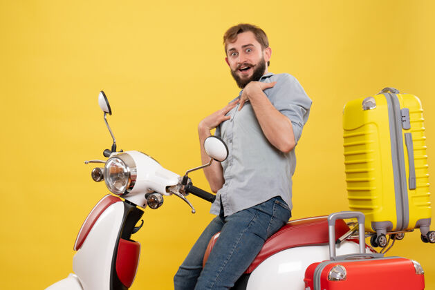 年轻人旅游概念与年轻的好奇胡须男子坐在摩托车上 并指出自己在它的黄色自己微笑车辆