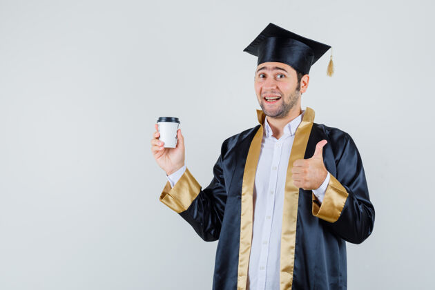 制服身着毕业制服的男青年端着一杯咖啡 竖起大拇指 神情高兴 俯视前方毕业男人男人