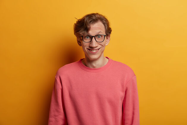 学生积极的时髦男人的孤立形象在最近的新闻上有愉快的反应 心情好 戴着眼镜出奇地看 穿着休闲的粉色套头衫 隔离在黄色的墙上真实的人类情感欧洲人风格模特