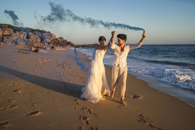 女性一对美丽的情侣在海滩上与蓝色烟雾弹合影的照片石头沙子海岸