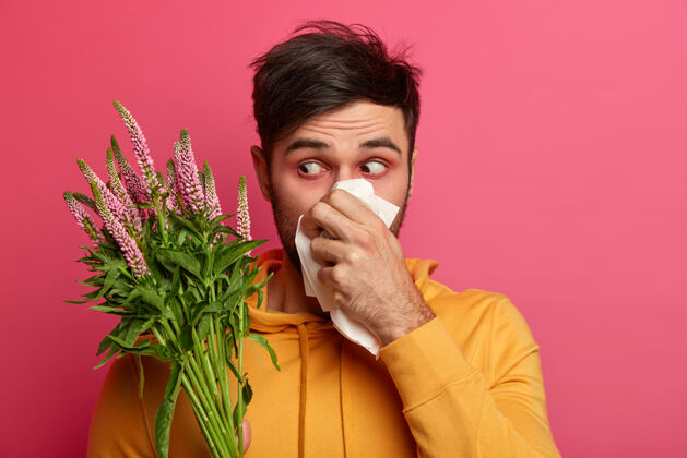 打喷嚏沮丧的人用组织吹鼻子 眼睛周围有红肿 过敏症状 有不健康的表情 集中在盛开的花朵上 患有鼻炎 过敏反应人与病阴性问题流涕