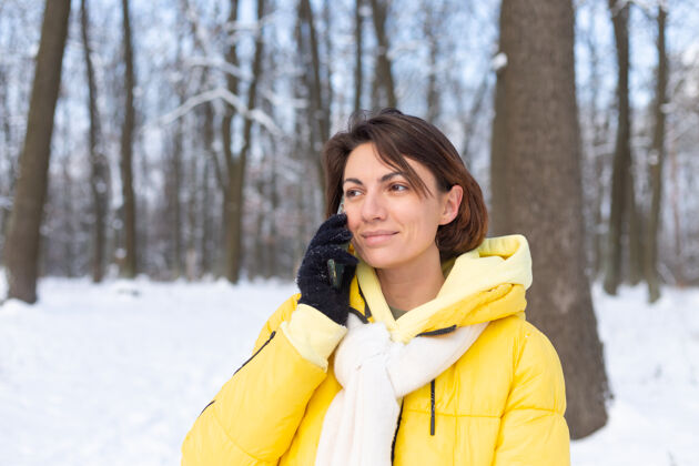 肖像心情愉快的快乐女人漫步在雪域的冬日森林里 愉快地聊着电话 享受着公园里的户外时光女士雪霜冻