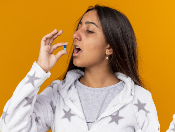 嘴巴年轻的生病女孩把药丸放进嘴里隔离在黄色背景上吃药女孩年轻