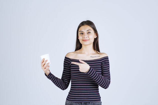 职员穿着条纹衬衫的女孩拿着一个塑料咖啡杯 介绍它是一种产品营销年轻人人类