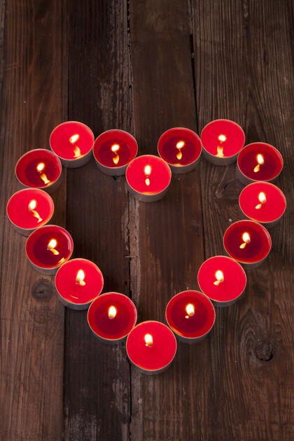 垂直垂直拍摄的红色和点燃的茶蜡烛形状像一个木头表面上的心表面情人节点燃
