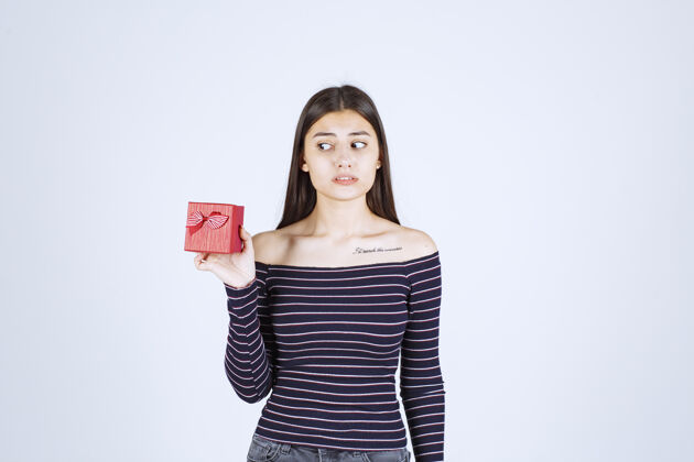 人体模特穿着条纹衬衫的女孩手里拿着一个红色的礼盒 看上去既困惑又怀疑聪明严重员工