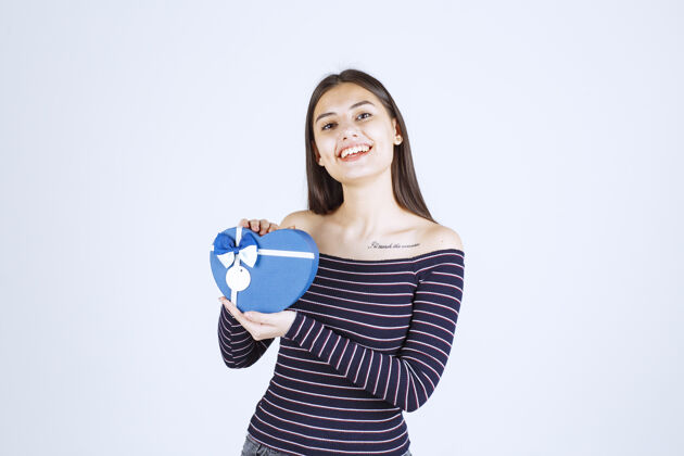 姿势穿着条纹衬衫的女孩手里拿着一个蓝色心形礼盒 微笑着休闲积极人体模特