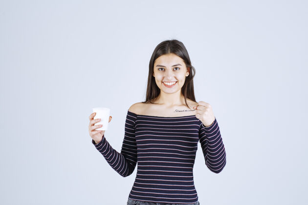 一次性穿着条纹衬衫的女孩拿着一个塑料咖啡杯 看起来很积极年轻雇员工人