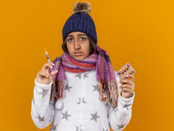 药丸悲伤的生病的年轻女孩戴着冬天的帽子戴着围巾拿着注射器拿着隔离在黄色背景上的药丸疾病围巾持有