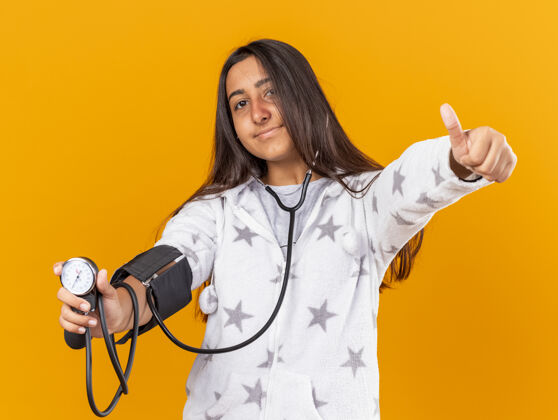 测量高兴的年轻病女孩测量自己的压力血压计显示拇指向上隔离在黄色背景年轻压力自己