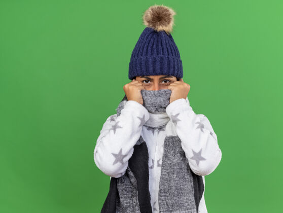 围巾年轻生病的女孩戴着带围巾的冬季帽子 脸上戴着围巾 看着镜头 隔离在绿色背景上 留着复印空间相机疾病封面
