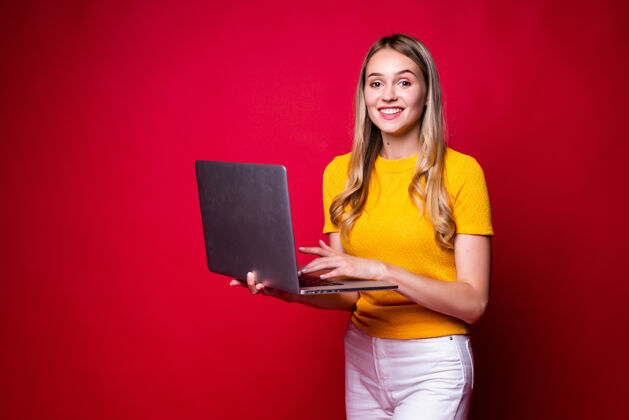 女性微笑的年轻女子手持笔记本电脑在红墙上工作脸笔记本电脑时尚