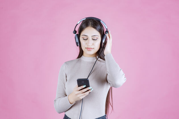 轨道戴着耳机在智能手机前放音乐的年轻女人娱乐模特年轻