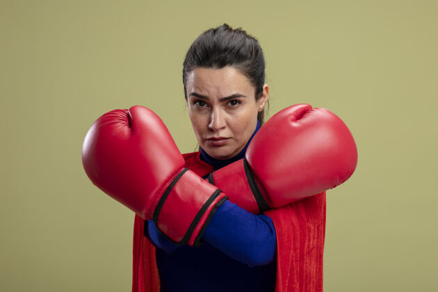 拳击自信的年轻超级英雄女孩戴着拳击手套双手交叉隔离在橄榄绿的背景手套超级英雄女孩