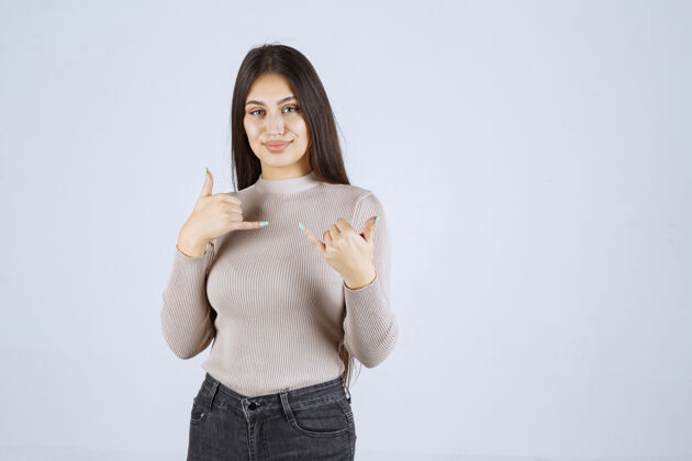 年轻穿灰色毛衣的女孩在做竖起大拇指的招牌雇员姿势人类