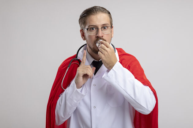 超级英雄年轻的超级英雄穿着医用长袍 戴着听诊器和眼镜 把听诊器放在嘴上 在白色背景上表现出沉默的手势沉默听诊器家伙