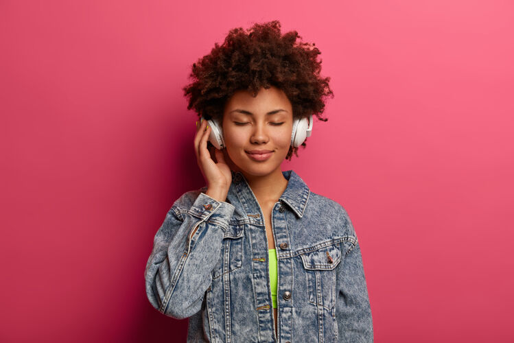 生活方式放松的卷发女人用新的立体声耳机听音乐站时髦罗西