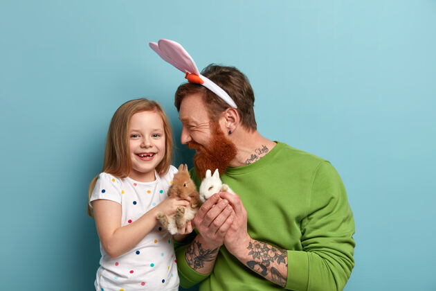 动物孩子和爸爸正和两只毛茸茸的兔子玩呢携带孩子胡子