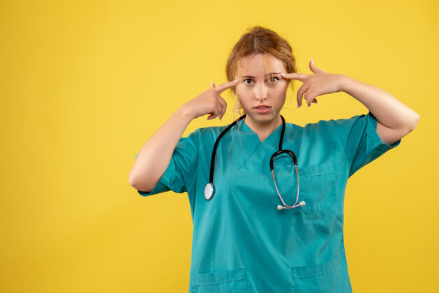 成人黄色墙壁上穿着带听诊器的医疗服的女医生的正视图医疗医生病毒