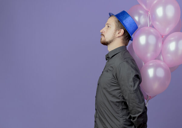 侧着戴着蓝帽子的帅哥站在一旁 紫色的墙上孤立着氦气球帅哥帽子男人