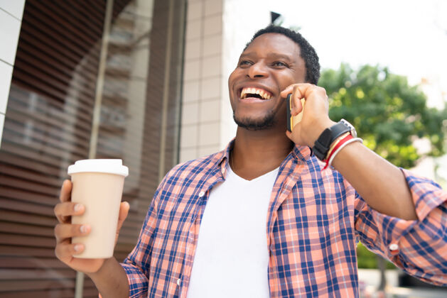 设备一个非洲裔美国人在街上散步时 手里拿着一杯咖啡 一边打电话电话一个外面