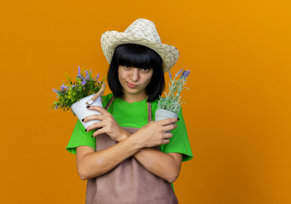 女自信的年轻女园丁穿着制服 戴着园艺帽 双手交叉握着花盆园艺花园信心