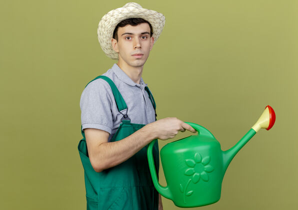 复制自信的年轻男园丁戴着园艺帽站在一边拿着浇水罐年轻男性立场