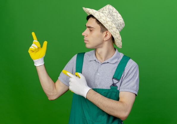 穿自信的年轻男园丁戴着园艺帽和手套看着并指着旁边壁板复制男