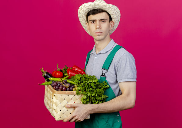 穿自信的年轻男园丁戴着园艺帽站在一旁 手里拿着菜篮子信心花园复制