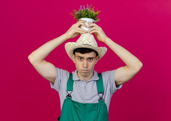 空间恼怒的年轻男园丁戴着园艺帽把花盆举过头顶花盆烦恼戴