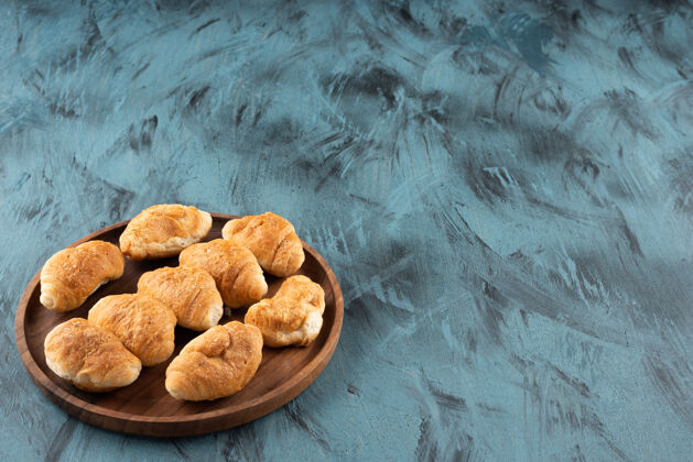 面包小甜羊角面包在深蓝色背景的木制盘子里泡芙甜点面包卷