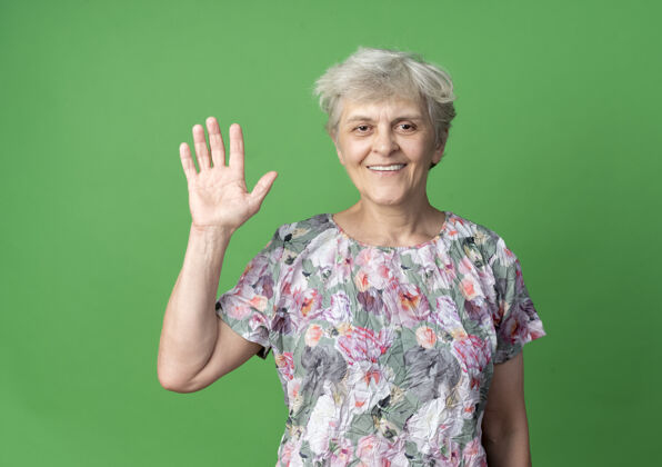 绿色微笑的老妇人在绿墙上举手举起来手微笑