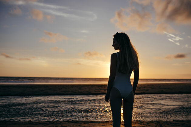 度假白种女人在度假时穿白色泳装无忧无虑的年轻女士在海边享受夜晚 看着美丽的日落海景地平线风景