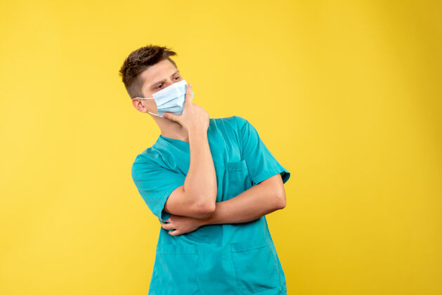 面具穿着医疗服 戴着无菌口罩的男医生的正面图黄色墙壁上的思考病毒健康快乐