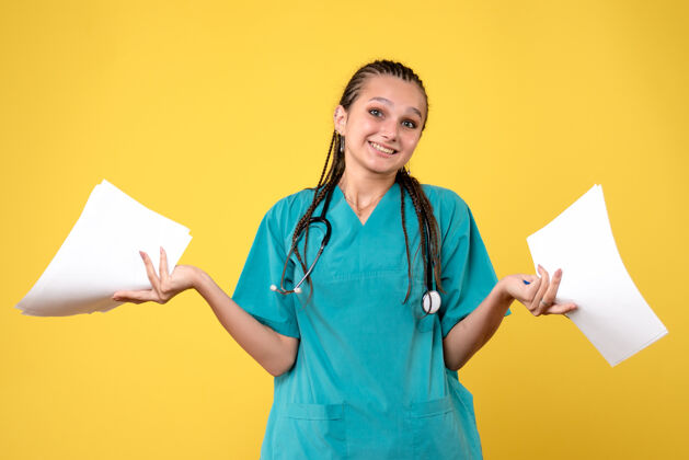 情绪黄墙上穿着医疗服拿着纸的女医生的正视图人女医生持有