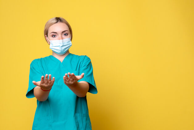 医院黄墙上年轻女医生穿着医用衬衫 戴着口罩的正面图大流行衬衫正面