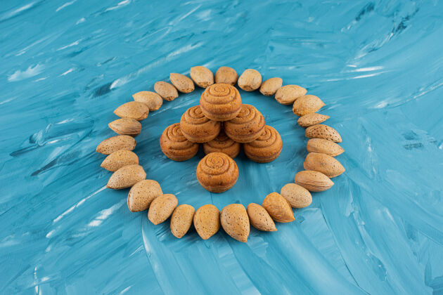 圆形一圈杏仁和新鲜甜甜的圆形饼干 背景是蓝色的生的种子美味