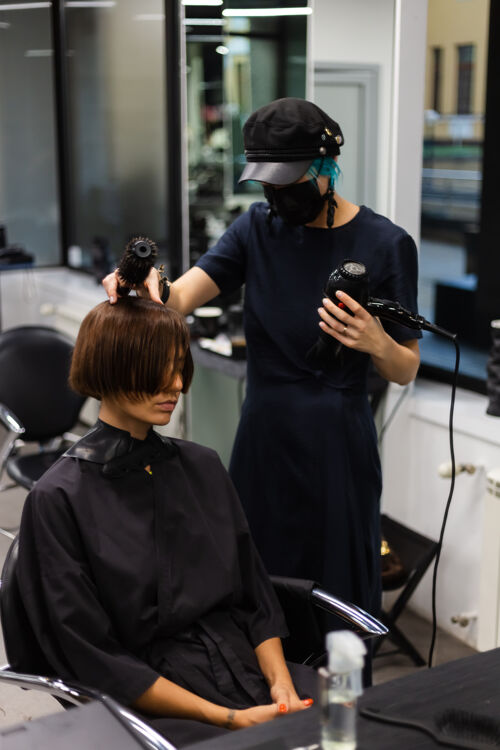 设备一个专业的女理发师给客户理发这个女孩戴着面具坐在美容院里脸人时尚