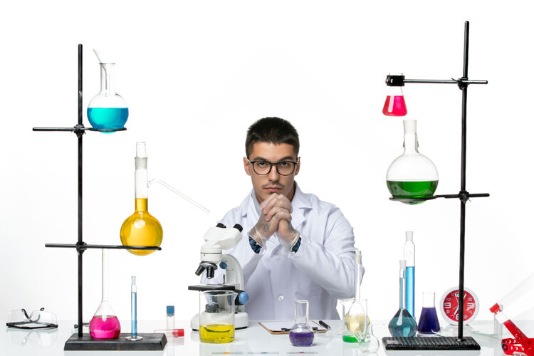 疾病正面图：身穿白色医疗服的男性化学家坐在白色背景的冠状病毒疾病病毒科学实验室里 拿着溶液视图科学容器