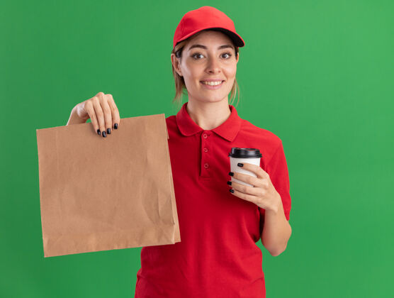 人高兴的年轻漂亮的女送货员穿着制服拿着纸包装和纸杯在绿色年轻包装制服