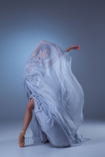 动作美丽的芭蕾舞演员在蓝色背景上穿着蓝色长裙跳舞丝绸活跃芭蕾舞