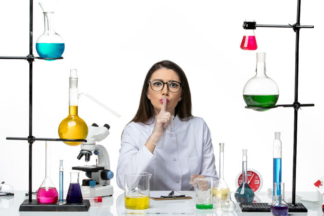 科学前视图穿着白色医疗服的女化学家正坐在白色背景上拿着解决方案科学大流行实验室病毒covid坐着套装个人