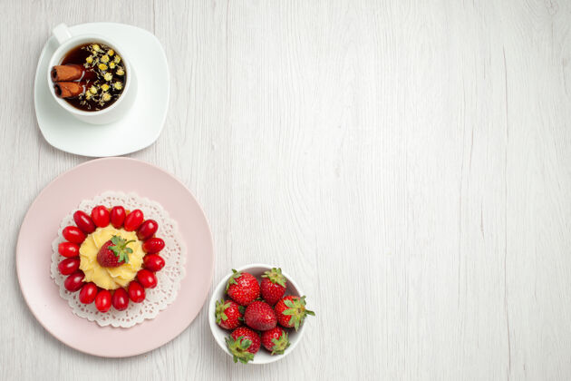 草莓俯瞰白色书桌上的奶油蛋糕和一杯茶饮食美味多汁