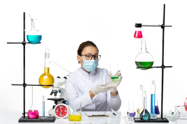 套装前视图穿着医疗服的女化学家 在浅白色背景上涂有面罩保持溶液 飞溅实验室病毒化学covid-面具实验室烧杯